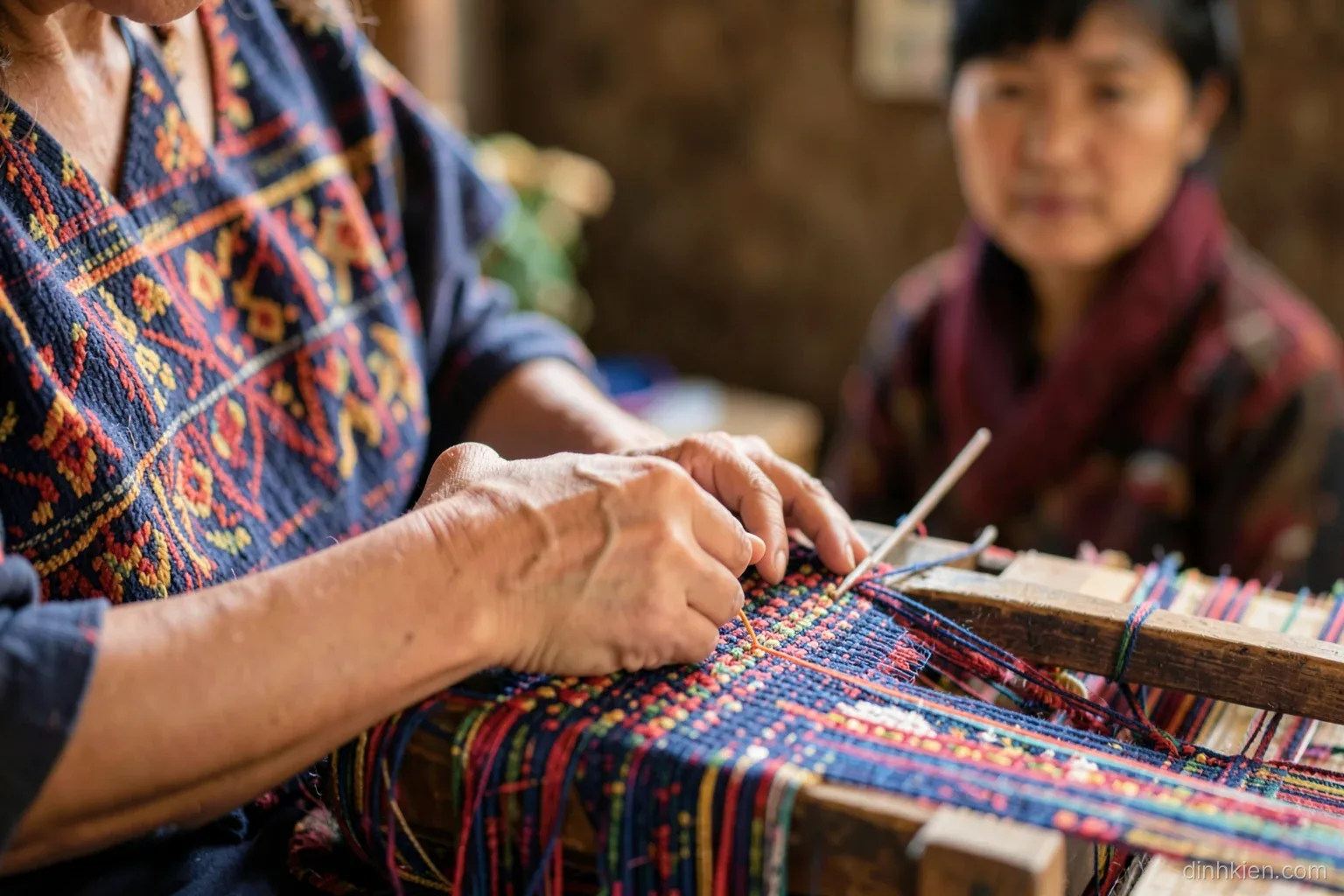 Close-up of hands of a Vietnamese highland artisan weaving colorful brocade on a wooden loom, a visitor watching respectfully in soft focus, warm daylight, rich indigo and red